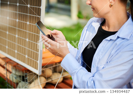 Happy woman using smartphone connected to solar panel. Cropped view. Integration of sustainable renewable energy into everyday life, demonstrating practical use of solar power for charging devices. Happy woman using smartphone connected to solar panel. Cropped view. Integration of sustainable renewable energy into everyday life, demonstrating practical use of solar power for charging devices. 134934487