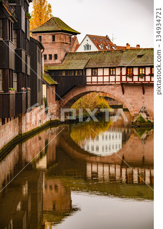 Historic Bridge And Medieval Architecture In Nuremberg: Traditional Half-Timbered Houses Reflected In Calm River Water On An Overcast Autumn Day Historic Bridge And Medieval Architecture In Nuremberg: Traditional Half-Timbered Houses Reflected In Calm River Water On An Overcast Autumn Day 134934721
