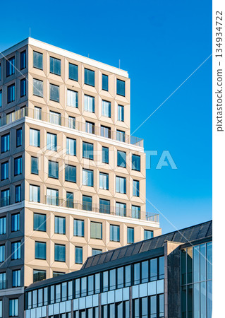 Modern Office Tower In Munich: Contemporary Urban Architecture With Geometric Facade And Glass Windows Under Clear Blue Sky Modern Office Tower In Munich: Contemporary Urban Architecture With Geometric Facade And Glass Windows Under Clear Blue Sky 134934722