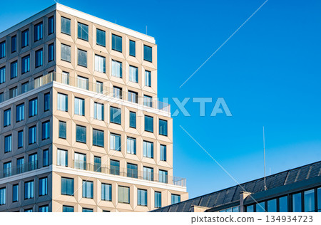 Modern Office Tower In Munich: Contemporary Urban Architecture With Geometric Facade And Glass Windows Under Clear Blue Sky Modern Office Tower In Munich: Contemporary Urban Architecture With Geometric Facade And Glass Windows Under Clear Blue Sky 134934723