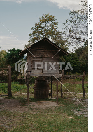 An old wooden barn stands on poles in the countryside, surrounded by trees and grass. An old wooden barn stands on poles in the countryside, surrounded by trees and grass. 134934766