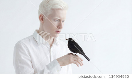Beautiful albino model holding a black crow in hands 134934930