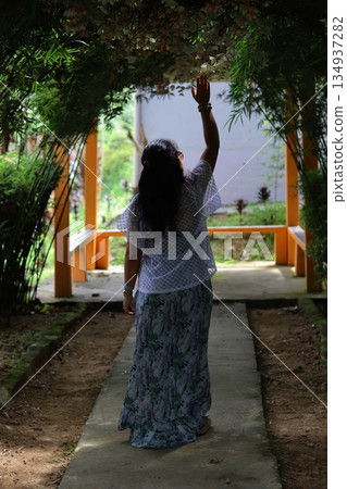 Woman walking along a garden pathway in Cameron Highlands, Malaysia, surrounded by lush plants and natural shade, expressing peaceful nature travel. Woman walking along a garden pathway in Cameron Highlands, Malaysia, surrounded by lush plants and natural shade, expressing peaceful nature travel. 134937282