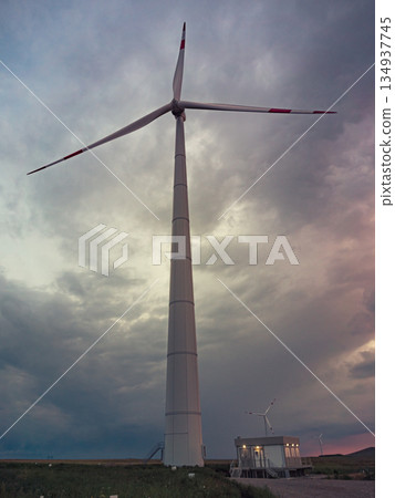 Bottom view of a tall wind turbine silhouette against dramatic sunset sky. 134937745