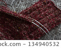 Cozy knitted socks on needles on grey background. Mix of red, green and white yarn on knitting needles. Knitting process of wool socks. Knitting hobby. Knitwear concept. Needlework background.  134940532