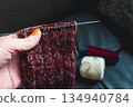 Woman holding cozy knitted socks on needles in hand. Mix of red, green and white yarn on knitting needles. Knitting process of wool socks. Knitting hobbies. Knitwear concept. Needlework background.  134940784