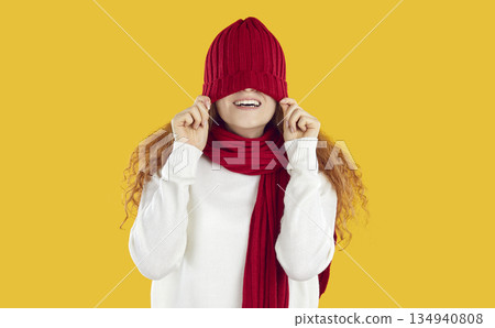 Funny teenage girl in scarf behaves cheerfully and playfully, pulling red warm hat on her eyes. Funny teenage girl in scarf behaves cheerfully and playfully, pulling red warm hat on her eyes. 134940808
