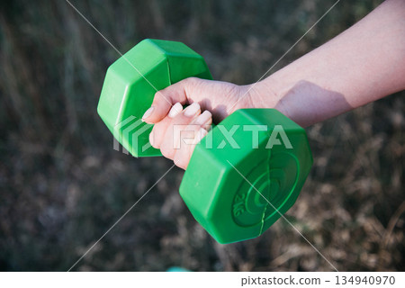 A woman doing dumbbell exercises outdoors. Outdoor sports. Green dumbbells in the athlete's hands.  134940970