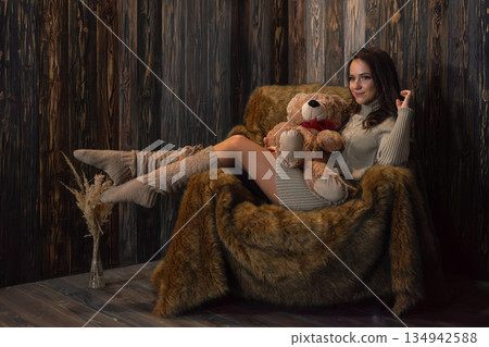 Woman sitting on a chair holding a teddy bear in a cozy indoor setting during winter Woman sitting on a chair holding a teddy bear in a cozy indoor setting during winter 134942588