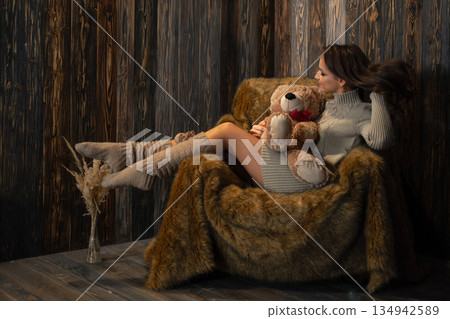 Cozy indoor scene of a woman sitting in a chair with a teddy bear during a quiet afternoon 134942589