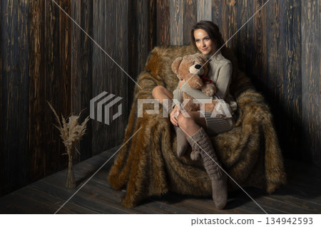 Woman sits on a fur chair holding a teddy bear in a cozy indoor setting during daylight hours 134942593
