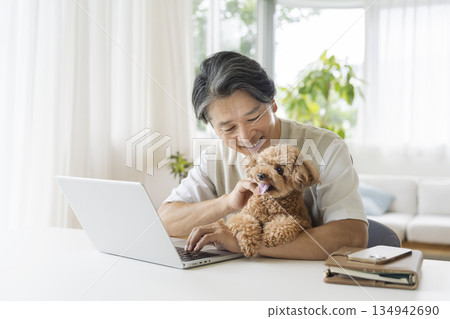 一位五十多歲的男子一邊用筆記型電腦工作，一邊抱著他的寵物狗 134942690