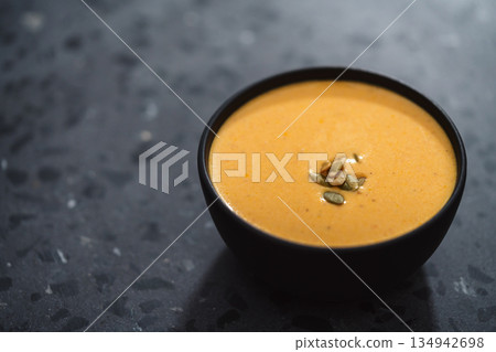 Pumpkin cream soup with pumpkin seeds in a black bowl on concrete background 134942698