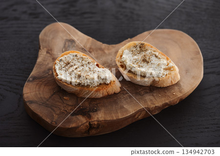 Ciabatta slices with cream cheese and herbs on olive wood board Ciabatta slices with cream cheese and herbs on olive wood board 134942703