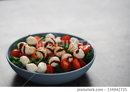 Salad with mozzarella, tomatoes and kale leaves in blue bowl on concrete countertop Salad with mozzarella, tomatoes and kale leaves in blue bowl on concrete countertop 134942725