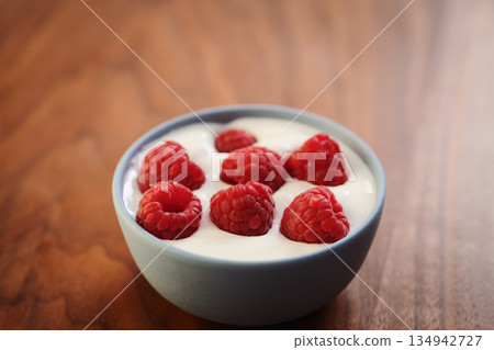 Yogurt with fresh raspberries in blue ceramic bowl on walnut table Yogurt with fresh raspberries in blue ceramic bowl on walnut table 134942727