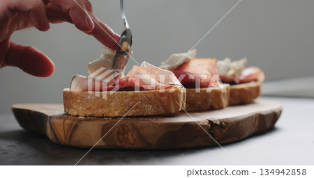 Slow motion man add ricotta to slice of ciabatta with fig marmalade and pancetta Slow motion man add ricotta to slice of ciabatta with fig marmalade and pancetta 134942858