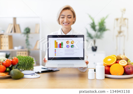 A nutritionist smiles while presenting a balanced diet plan on a laptop, surrounded by fresh fruits and vegetables. A nutritionist smiles while presenting a balanced diet plan on a laptop, surrounded by fresh fruits and vegetables. 134943138