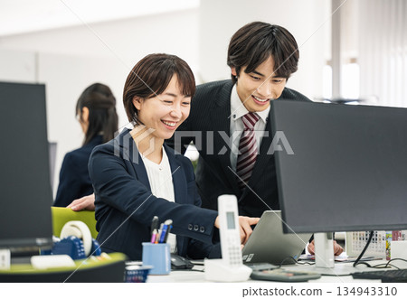 Young male and female business people working together while looking at a computer screen in an office Young male and female business people working together while looking at a computer screen in an office 134943310