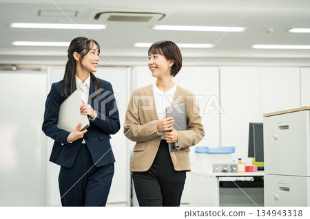 一位年輕的職業婦女在辦公室裡邊走邊和同事聊天。 134943318