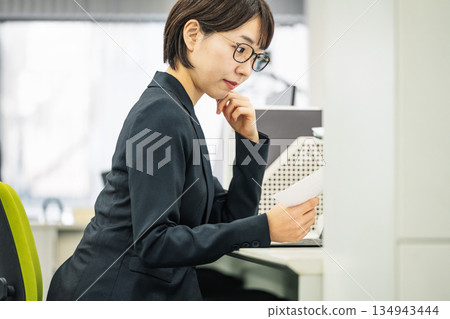 年輕女子在辦公室裡一邊看著文件一邊思考。 134943444