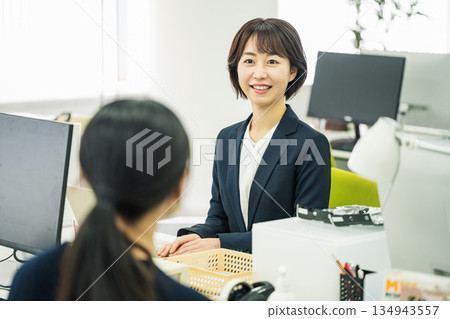 Young woman talking to her colleague at her desk in the office 134943557