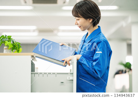A young woman in work clothes taking out a file in the office 134943637