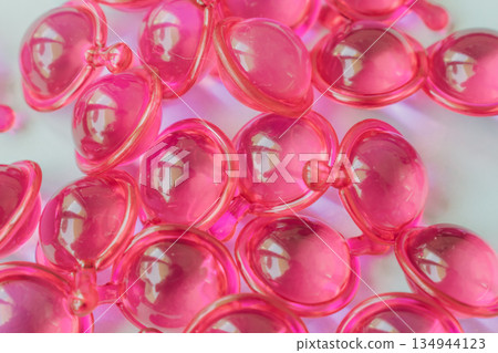 Close-up macro shot of many glossy pink hair treatment capsules. Focused foreground highlights the rich oil and reflective texture Close-up macro shot of many glossy pink hair treatment capsules. Focused foreground highlights the rich oil and reflective texture 134944123