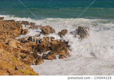 Sea foam crashing against rocky shore. 134944129