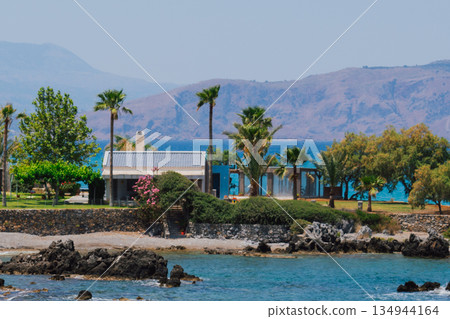 Picturesque landscape from the paradise Greek island of Crete. Cozy house by the sea surrounded by palm trees and greenery 134944164