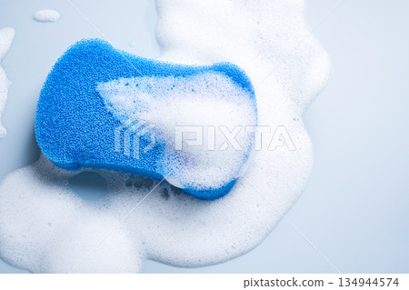 Blue sponge surrounded by white soap foam on pale blue background Blue sponge surrounded by white soap foam on pale blue background 134944574