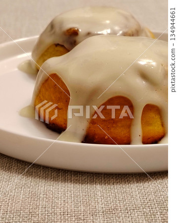 Cinnamon rolls with white icing glaze on a plate. 134944661