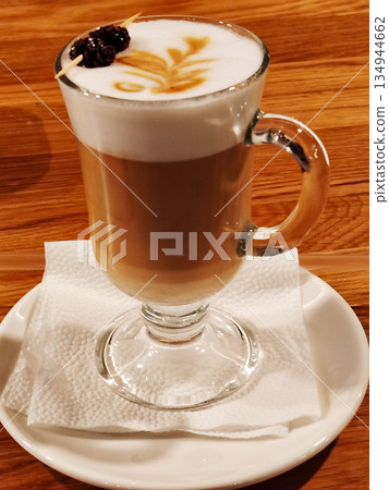 Latte coffee with milk foam art and pine cone garnish in glass. Latte coffee with milk foam art and pine cone garnish in glass. 134944662