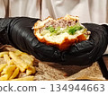Hands in black gloves holding a juicy bitten burger. 134944663