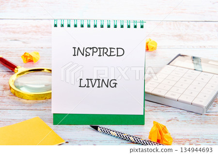 A vibrant scene showcases a notepad with the words INSPIRED LIVING alongside a magnifying glass, calculator, and pencil on a rustic wooden surface, hinting at mindful intention 134944693