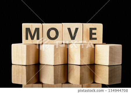 Wooden toy blocks are arranged in a stack, spelling out the word MOVE. The arrangement sits atop a reflective surface in front of a dark, seamless background Wooden toy blocks are arranged in a stack, spelling out the word MOVE. The arrangement sits atop a reflective surface in front of a dark, seamless background 134944708