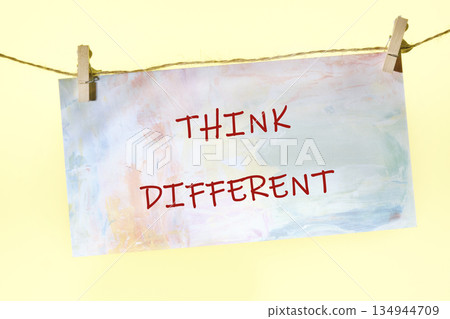 A colorful paper with the words Think Different written in red ink hangs by clothespins on a string. The paper has a painted watercolor effect A colorful paper with the words Think Different written in red ink hangs by clothespins on a string. The paper has a painted watercolor effect 134944709