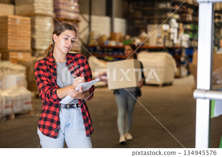 Female manager leads the accounting of materials in large warehouse 134945576