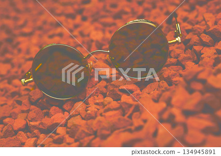 Blurred smooth vintage cool gold sunglasses on pebbles red stones Blurred smooth vintage cool gold sunglasses on pebbles red stones 134945891