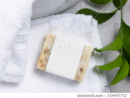 Soap with blank label on white bath towel near basin and green leaves on grey stone, mockup Soap with blank label on white bath towel near basin and green leaves on grey stone, mockup 134947732