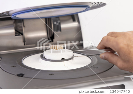 Orthodont men puts tooth implants into dental ceramic oven for baking enamel. Dental prosthetics Orthodont men puts tooth implants into dental ceramic oven for baking enamel. Dental prosthetics 134947740