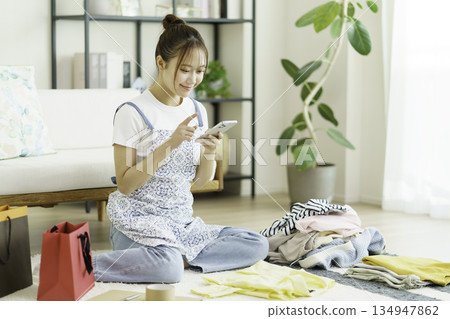 A young woman taking photos of clothes with her smartphone in her room. Mercari Auction 134947862