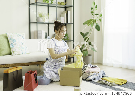 A young woman packing clothes into cardboard boxes in her room 134947866