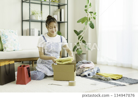 A young woman packing clothes into cardboard boxes in her room A young woman packing clothes into cardboard boxes in her room 134947876