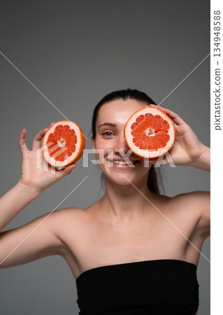 Close-up portrait of woman with grapefruit slice, minimalist beauty concept highlighting skincare, freshness, vitamins and healthy lifestyle 134948588