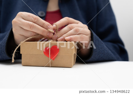 Woman is Tying a Valentine's Day Present With Twine and a Red Heart 134948622