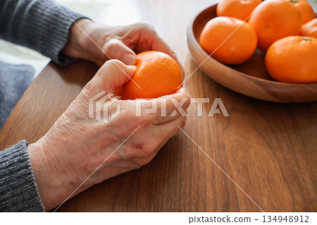 Elderly woman's hands holding a mandarin orange on a wooden table 134948912