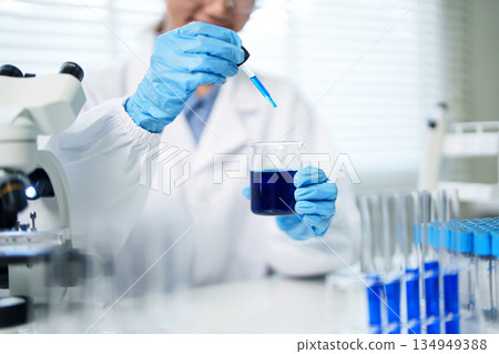 Scientist adult expert hand working chemistry experiment lab microscope beaker solution dropper analysis research development medical discovery innovation pharmaceutical 134949388