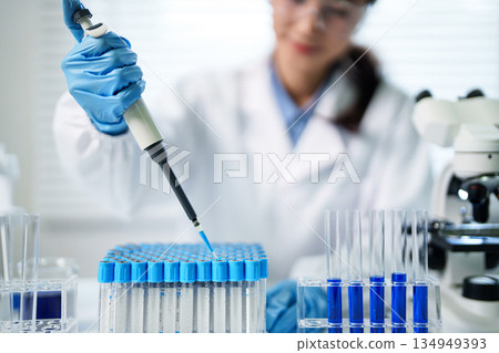 Asian adult female scientist conducting precision liquid transfer using micropipette for medical research and biotechnology analysis in a modern laboratory setting 134949393