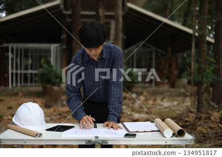 Civil engineer or site manager reviewing construction blueprints outdoors on a construction site. 134951817